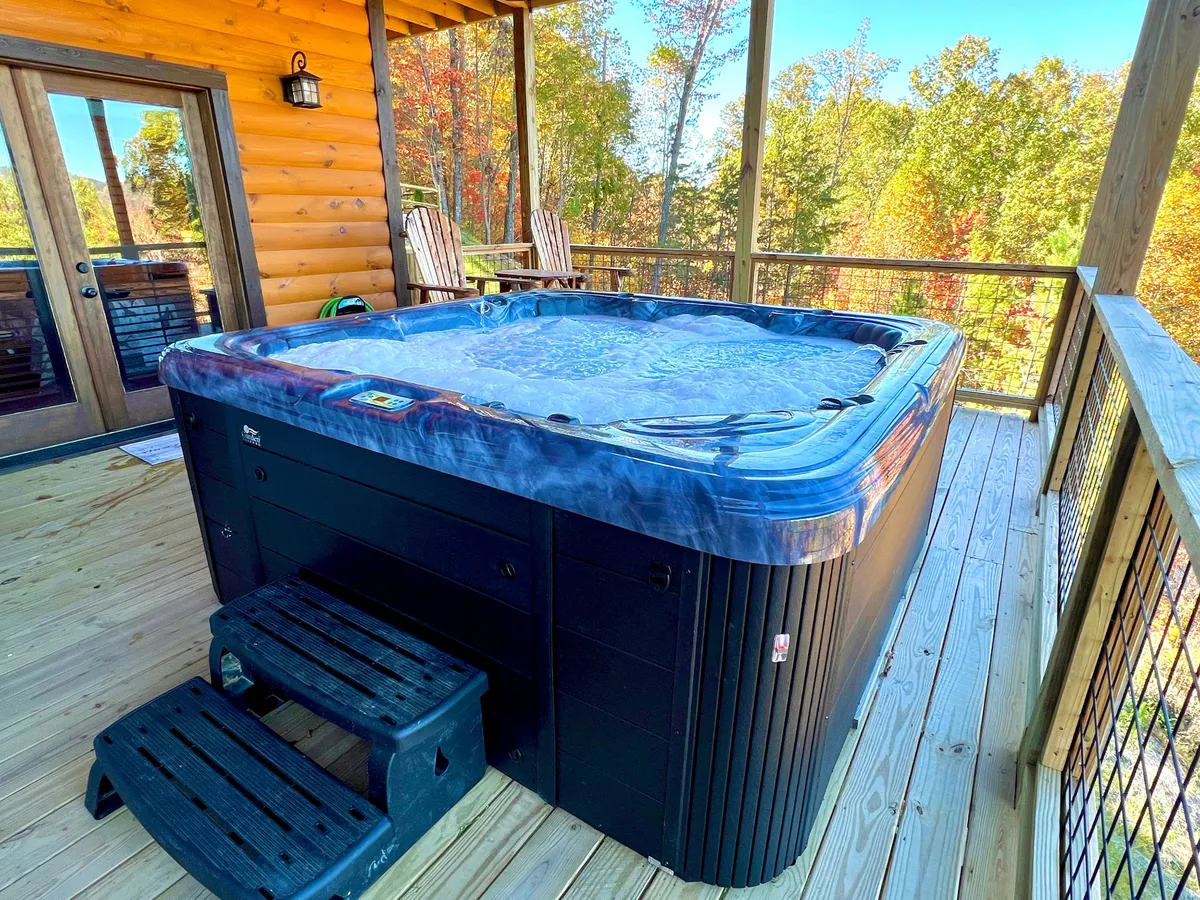 This image showcases a steaming hot tub on a wooden deck, surrounded by lush trees and Adirondack chairs, inviting guests to relax and socialize while immersed in nature. The tranquil mountain atmosphere and communal outdoor setting create an ideal backdrop for group bonding after a day of activities.