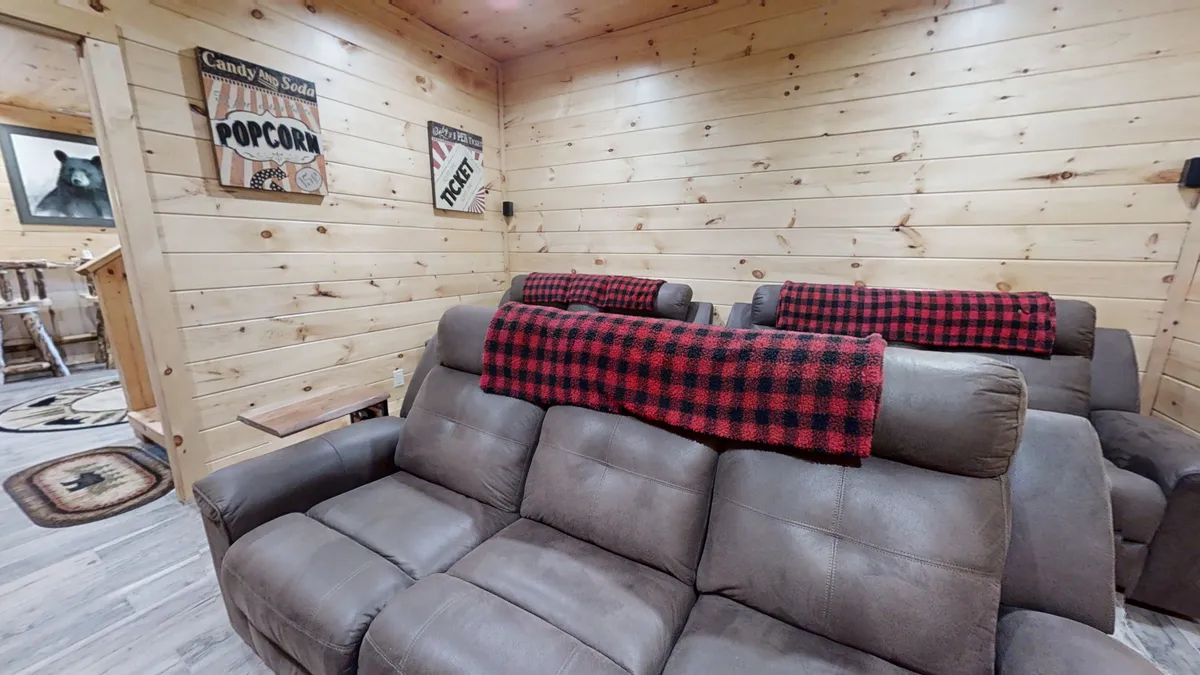 A comfortable living space with leather recliners, red plaid blankets, and wooden wall décor. The oversized TV serves as a focal point for movie nights or game sessions with friends and family.