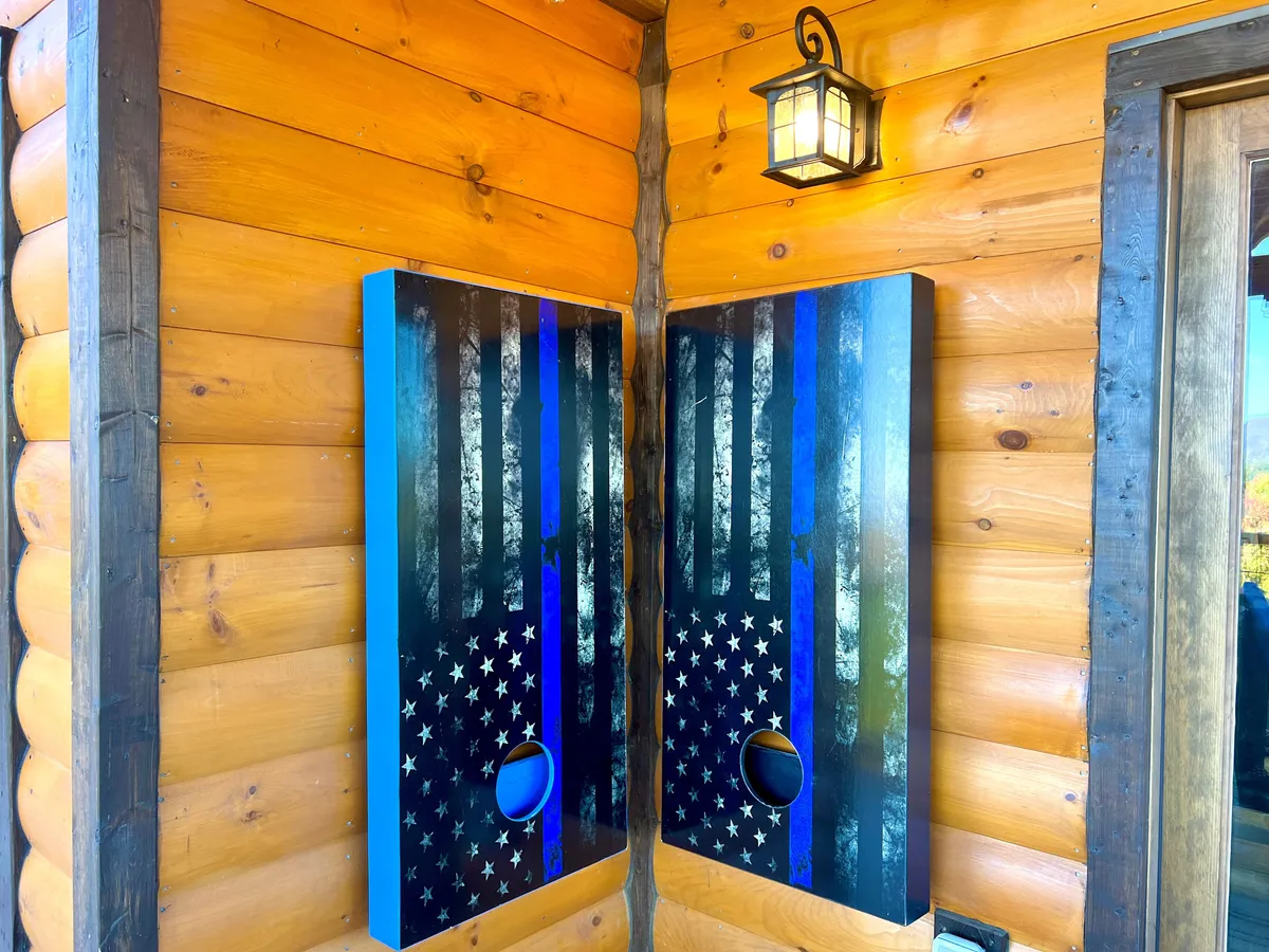 This playful exterior shot captures decorative cornhole boards set up outside a rustic log cabin. The setup suggests outdoor games, social gatherings, and lighthearted competition—ideal for large groups or families.