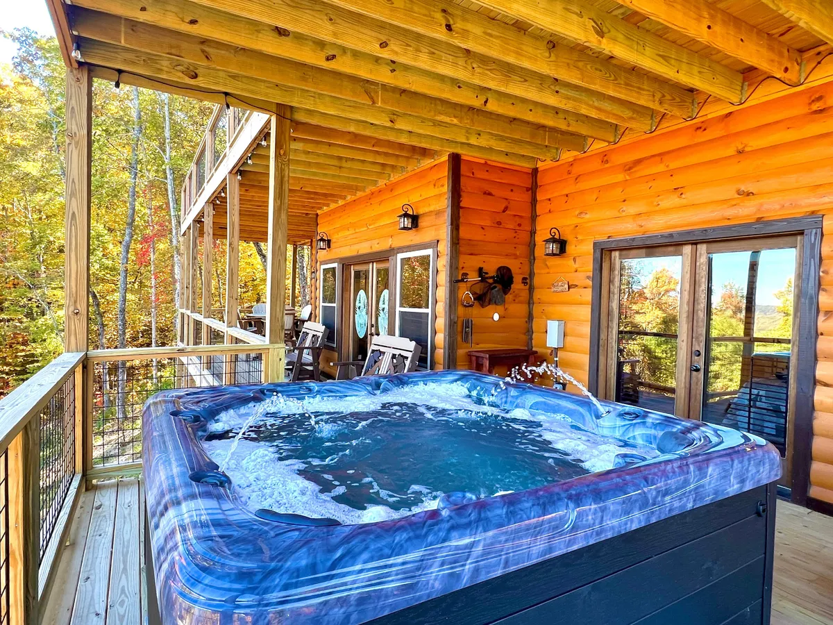 A tranquil outdoor setting featuring a private hot tub on a wooden deck, nestled against the log cabin’s structure with surrounding trees offering privacy and a beautiful natural backdrop. The scene exudes relaxation and exclusivity, perfect for unwinding while immersed in mountain views and forest tranquility.