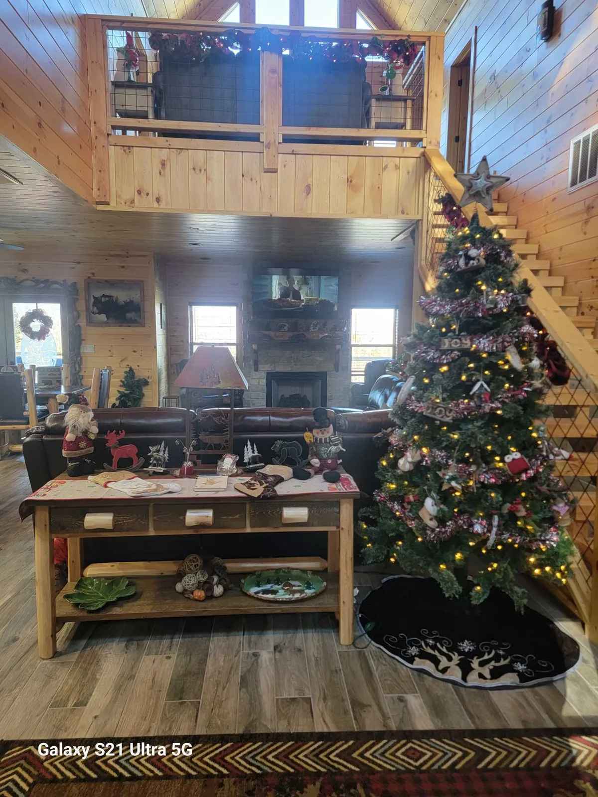 A cozy, festively decorated living area featuring a Christmas tree, a warm fireplace, a wooden table, and a sofa. The intimate setting is ideal for family gatherings, holiday celebrations, and enjoying the lodge’s fireplace in winter months.
