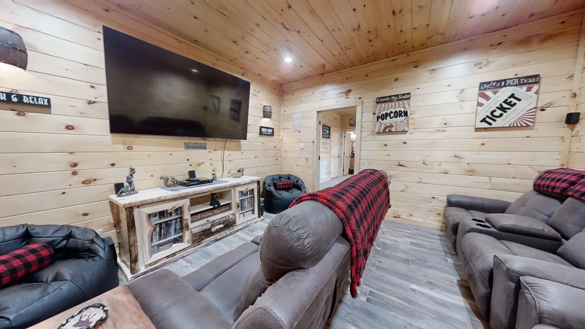 A cozy, inviting entertainment room with a large flat-screen TV, rustic wooden furniture, and plush seating. The space radiates warmth with decorative signs and soft lighting, perfect for group gatherings. The arrangement encourages socializing and creates a welcoming environment for activities like movie nights and game playing.