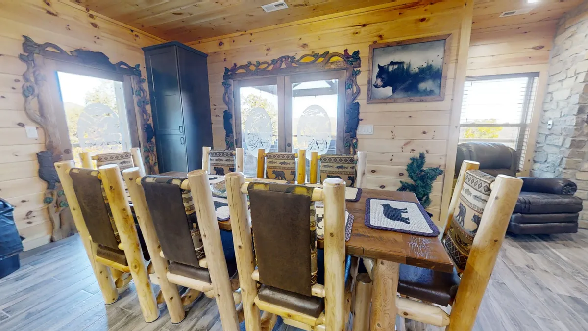 A rustic dining table with log-style chairs set in front of expansive windows offering scenic mountain views. The cozy ambiance is accentuated by decorative mirrors and natural wood elements, making it a perfect spot for family dinners or celebrations.