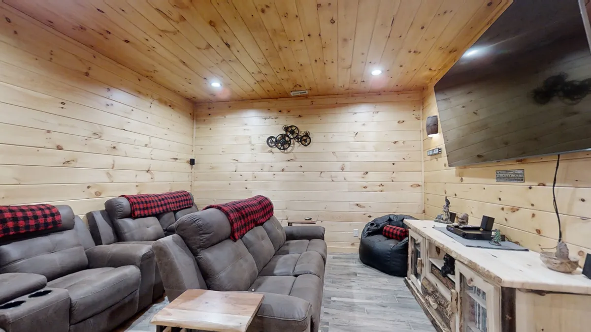 A relaxed family room featuring reclining sofas, wood paneling, a large TV, and accent pillows. The setting is ideal for group gatherings, game nights, or watching films together. The layout offers both comfort and a sense of togetherness, with ample seating for all ages.