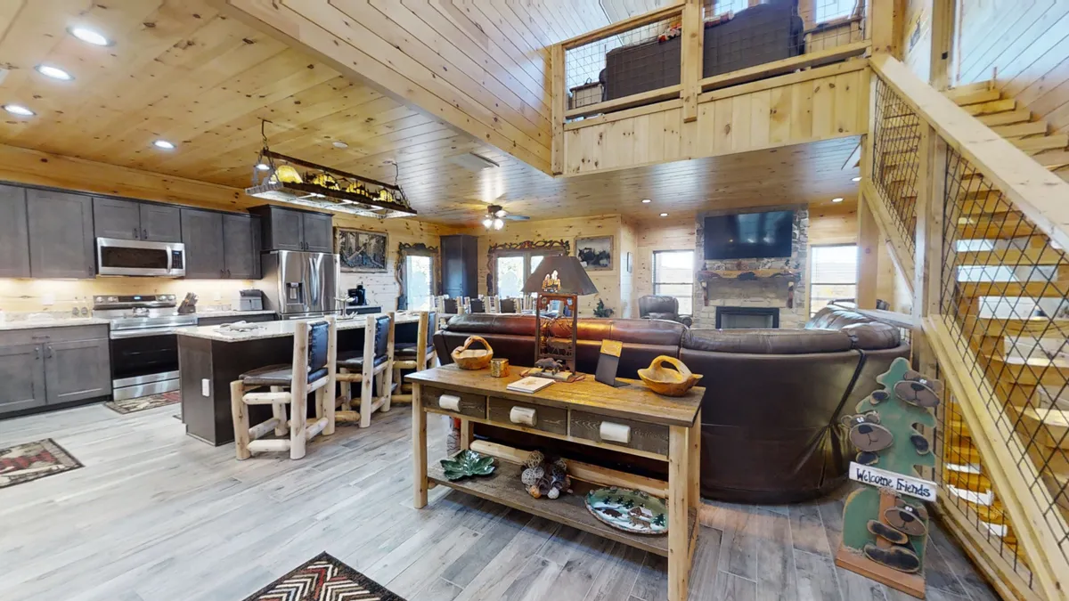 A bright, inviting kitchen with a large central island, adjacent to a comfortable sofa seating area. The staircase to the loft adds architectural interest, and the space is filled with natural wood textures, modern appliances, and a layout designed for both cooking and socializing.