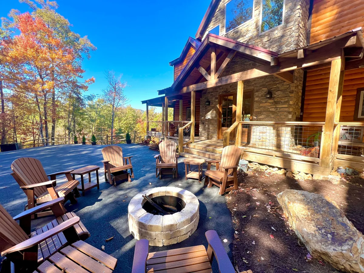 A cozy fire pit, encircled by Adirondack chairs, is nestled beside a rustic cabin structure and surrounded by rich autumn foliage. The scene evokes communal evenings spent storytelling, roasting marshmallows, or stargazing with loved ones.